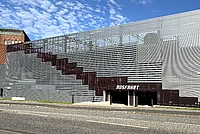Parkhaus mit wellenförmiger Metallfassade und großer Treppe an der Seite, darunter eine Ausfahrt