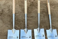 Vier Spaten mit Holzstielen und Metallspitzen stehen nebeneinander im Sand, auf den Klingen steht 'HAMBAG16 2026' und 'Johannes baut Jobs Berlin Hamburg Airport'