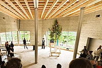 Menschen stehen im Kreis in einem großen Raum mit sichtbarer Holzbalkendecke um einen geschmückten Richtbaum auf einem Podest