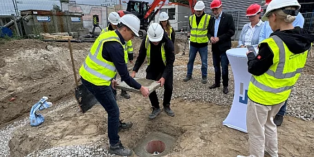 Noch kann man die Kapsel kurz sehen, dann vielleicht erst wieder in 1000 Jahren.... Mehrere Personen mit Schutzhelmen und Warnwesten stehen um eine geöffnete Grube auf einer Baustelle.