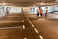 Besucher-Schnappschuss im 2 °C kühleren und sowieso coolen Parkhaus! Drei Männer stehen in einem Parkhaus auf dem Asphalt neben markierten Parkplätzen und unter einer Betondecke