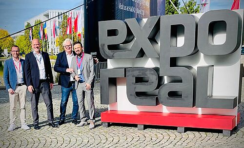 (v.l.n.r.) Steffen Blaser, Matthias Millow, Andreas Palla und John Frank neben dem Expo Real Logo
