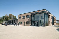 Modernes zweigeschossiges Gebäude mit großer Glasfassade und Backsteinmauerwerk bei sonnigem Wetter