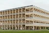 Mehrstöckiges Parkhaus aus Holz mit offenem Fassadendesign, umgeben von Wiesen und Bäumen.