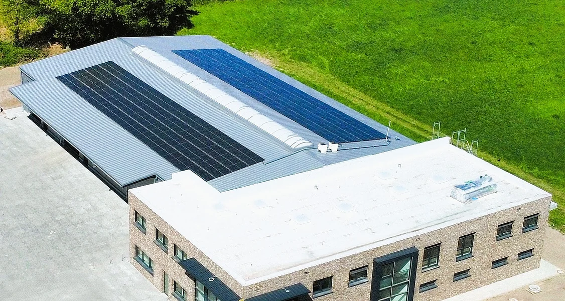Vollklinker im Bürotrakt und Isopaneelen im hinteren Hallenbereich Luftaufnahme eines modernen zweigeschossigen Gebäudes mit Flachdach und Solarpaneelen auf dem Nebendach, umgeben von grüner Wiese und Bäumen
