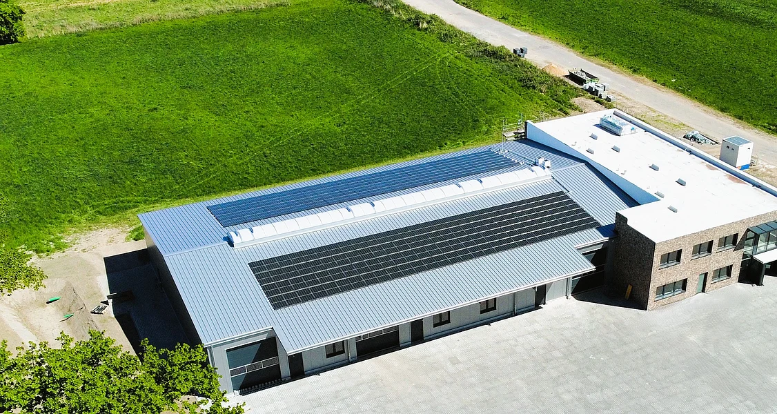 Auf dem Satteldach die PV-Anlage zur Selbstversorgung des Klebetechnikunternehmens Luftaufnahme eines modernen Gebäudekomplexes mit Solarpaneelen auf dem Dach und umgeben von Grünflächen